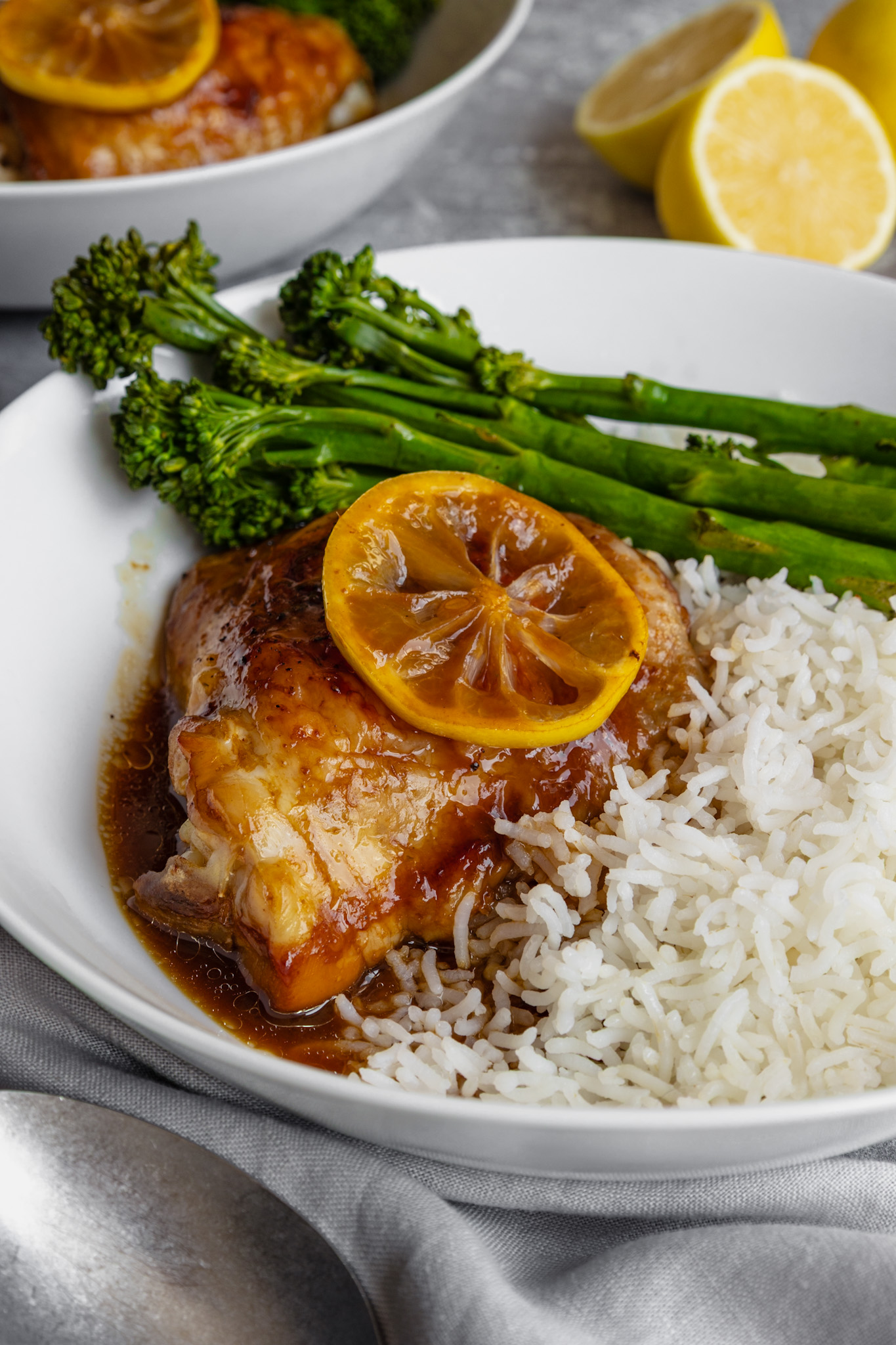 One lemon soy chicken thigh in a dish served with rice and tender broccoli