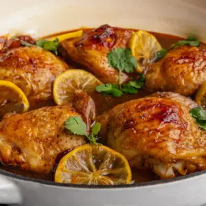 Lemon Soy Chicken Thighs In a casserole dish with slices of lemon and coriander sprigs