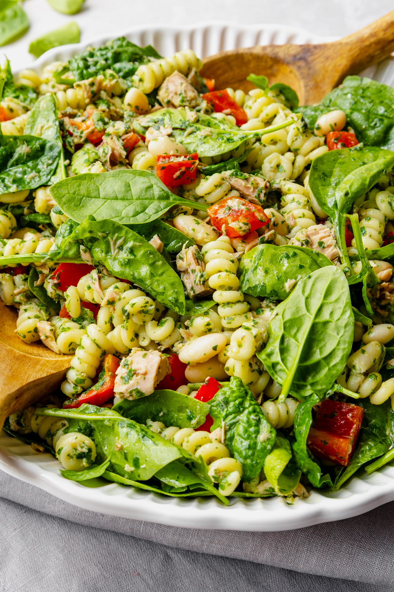 Tuna pasta salad with basil and parsley dressing in a dish with salad servers